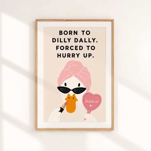 A framed art print featuring a minimalist illustration of a woman with pink hair, black sunglasses, and a yellow-orange face, holding a pink heart-shaped mirror. The text reads, 'BORN TO DILLY DALLY.