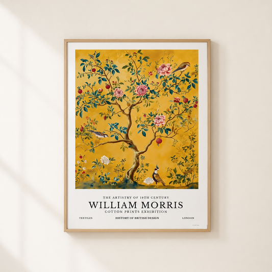 A framed William Morris art print featuring a decorative tree with pink flowers, birds, and red fruit on a mustard-yellow background, mounted on a warm off-white wall with soft window-shadow lighting.