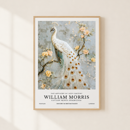 A framed art print featuring a white peacock with blue and gold feather details, set against a light gray floral background with peach blossoms. The print includes text at the bottom reading 'William Morris Cotton Prints Exhibition.