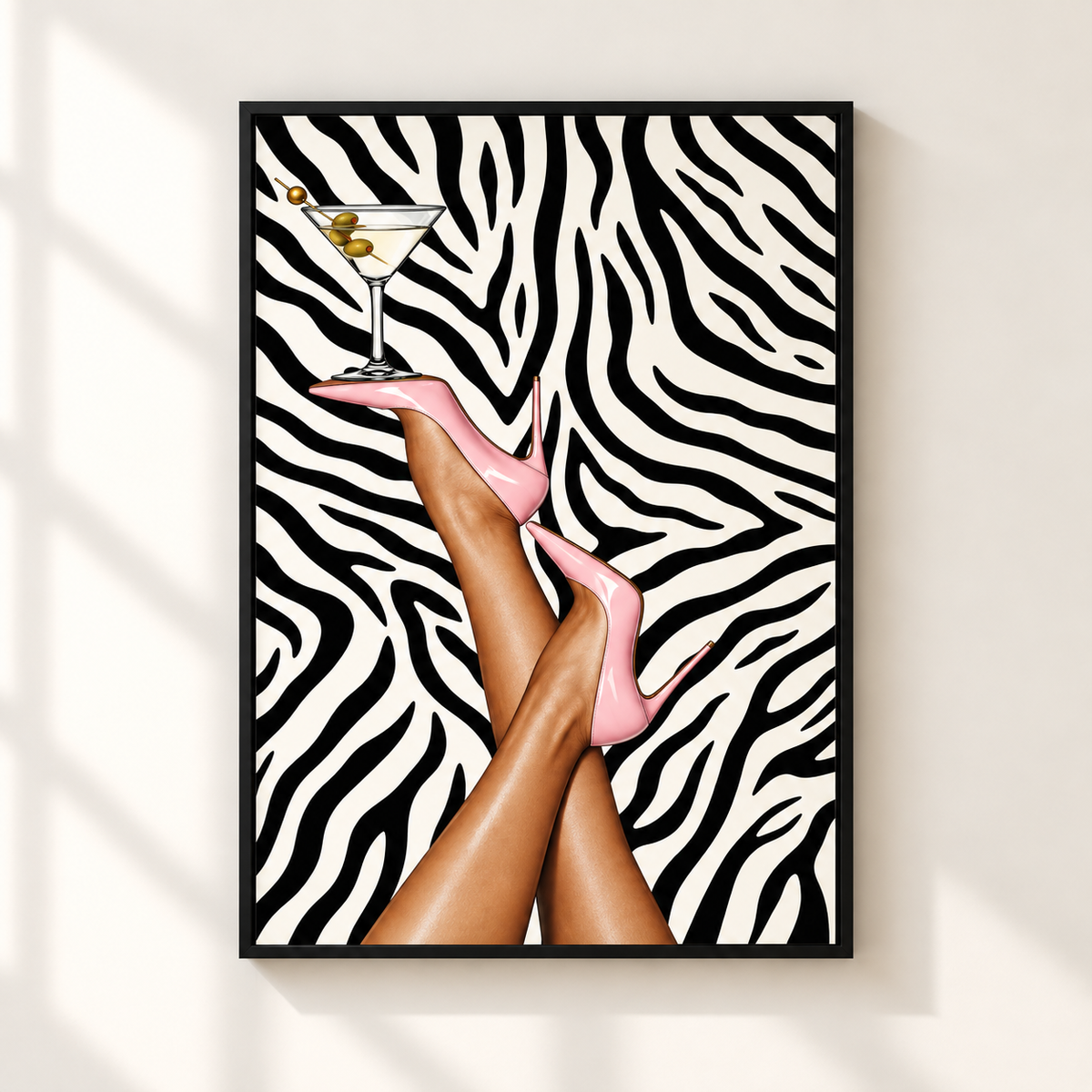 A framed art print featuring a zebra-stripe background with crossed legs wearing pink high heels and a martini glass, displayed on a light beige wall with soft window shadows.