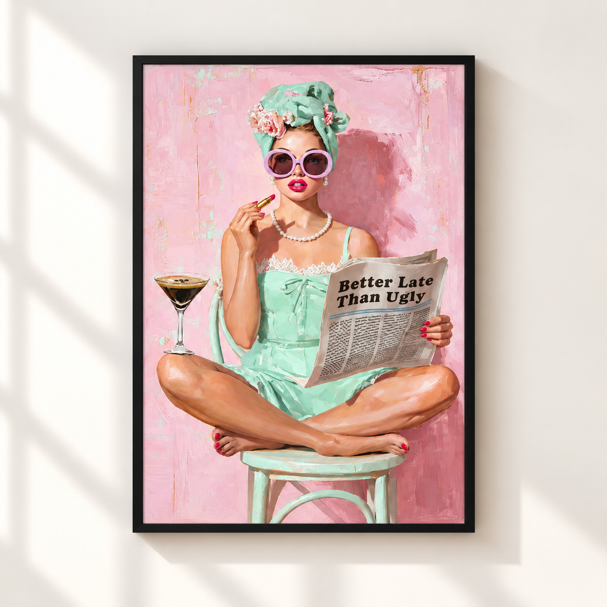 A framed art print featuring a retro-style illustration of a woman in a mint green dress and floral headwrap, sitting on a stool and reading a newspaper that says 'Better Late Than Ugly.' The print is displayed on a light wall with soft window shadow overlays.