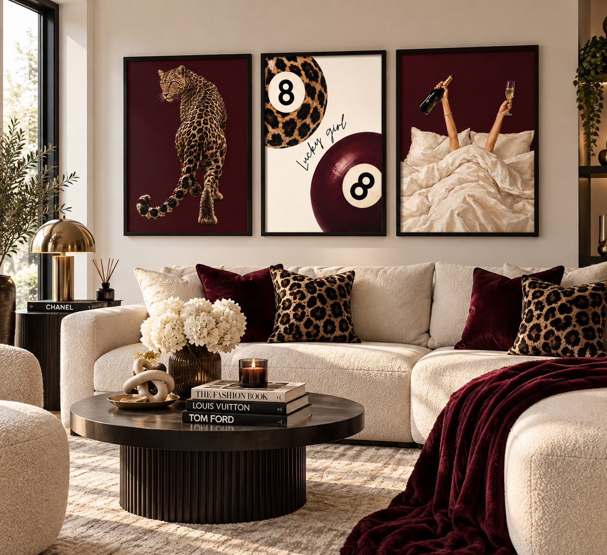 A styled living room featuring a three-panel framed wall art set above a cream sectional sofa. The artwork includes a leopard on a burgundy background, a split design with leopard print and an 8-ball, and legs in bed with champagne bottles and an 8-ball.