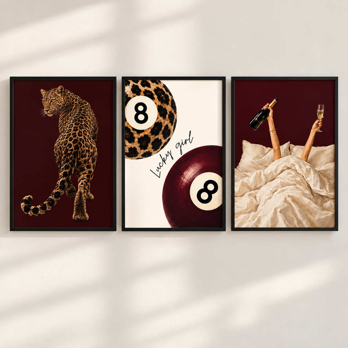 Three framed wall art prints hang side by side on a light wall with soft shadow overlays. The left print shows a leopard on a dark burgundy background.