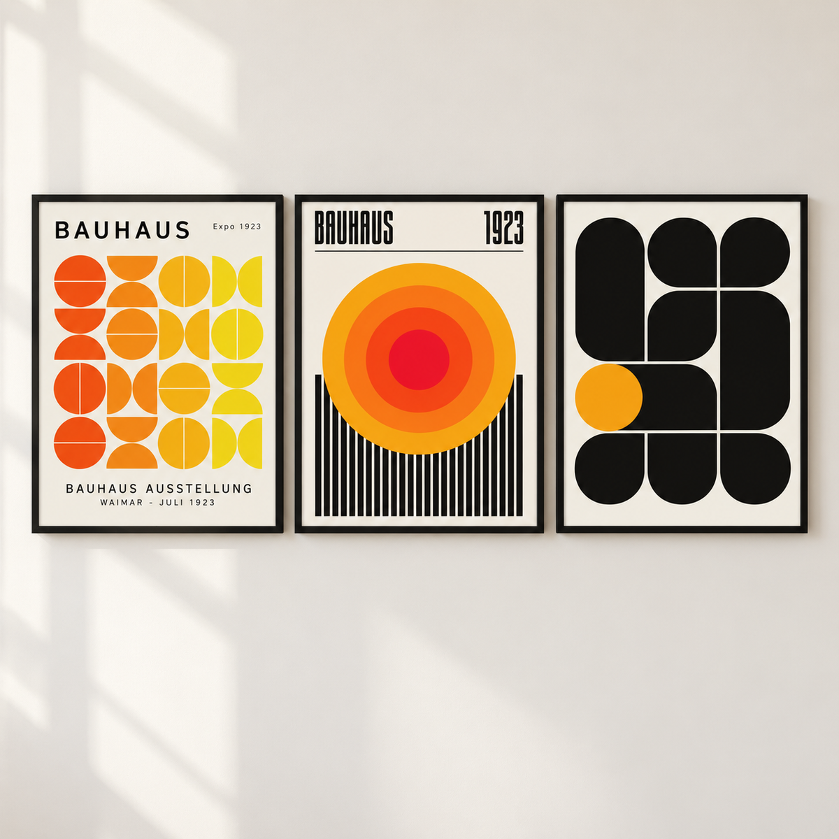 Three framed Bauhaus-style art prints hanging on a light wall, featuring bold geometric shapes and typography in orange, yellow, red, black, and white.