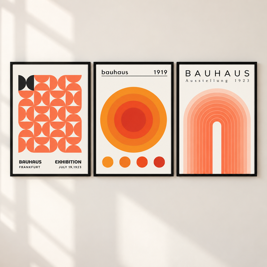 Three framed Bauhaus-style art prints hang side by side on a light beige wall with soft window shadows. The prints feature bold geometric and circular designs in orange, coral, yellow, and red on white backgrounds, with the word 'BAUHAUS' visible on two of the frames.