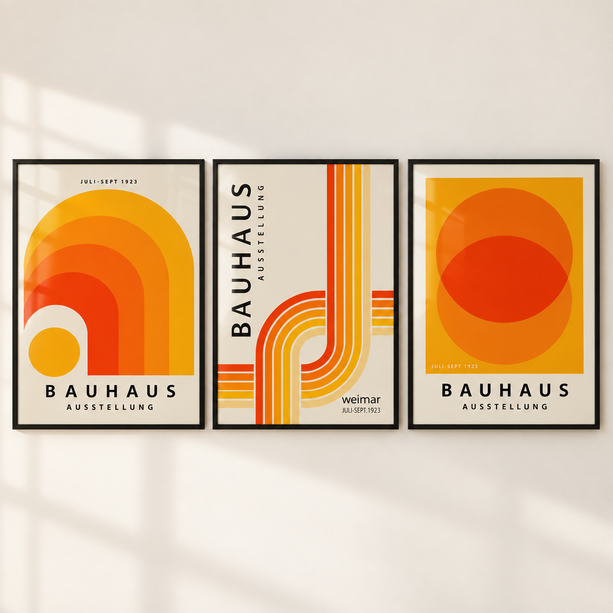 Three framed Bauhaus-style art prints with bold orange, yellow, and red geometric designs hang side by side on a light beige wall.