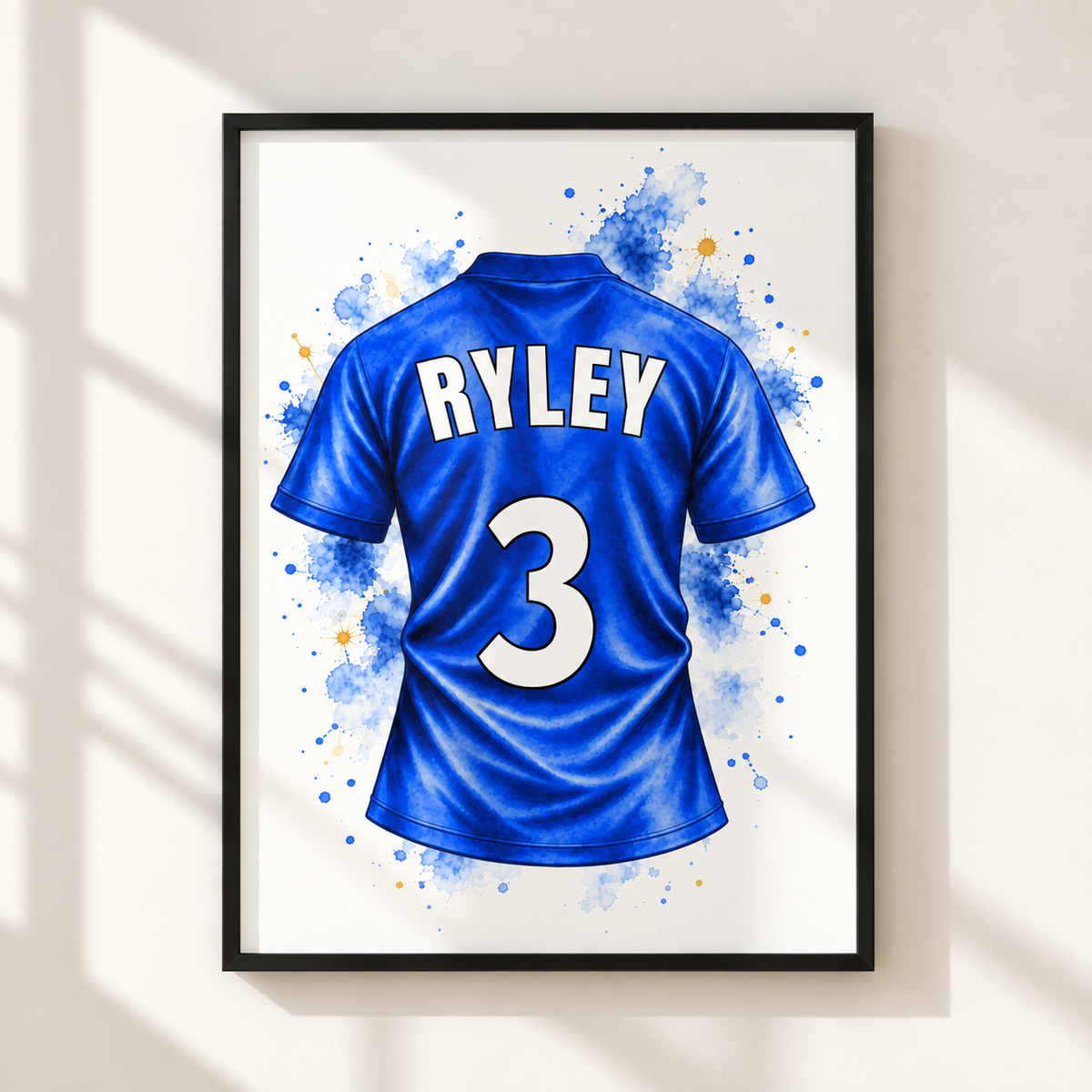 A framed wall art print showing the back of a blue soccer jersey with the name RYLEY and number 3, displayed on a light beige wall with soft window shadows.