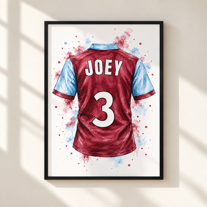 A framed watercolor-style print of a football jersey back, with the name JOEY and number 3 in white, set against splashes of red and blue on a white background. The frame hangs on a light beige wall with soft window-shadow lighting.