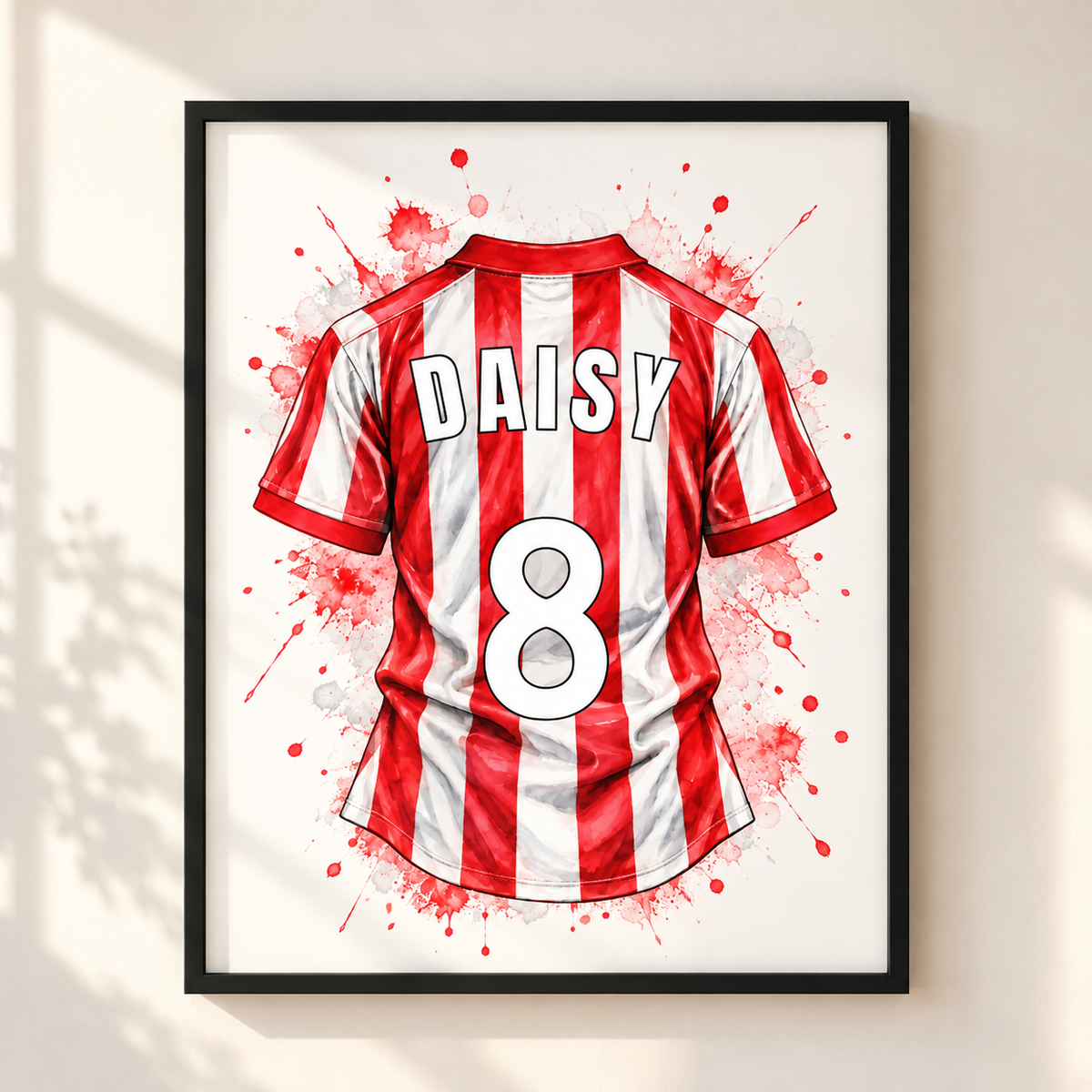 Framed wall art featuring a stylized red and white striped soccer jersey with the name DAISY and number 8, shown hanging on a light beige wall with soft window shadows.