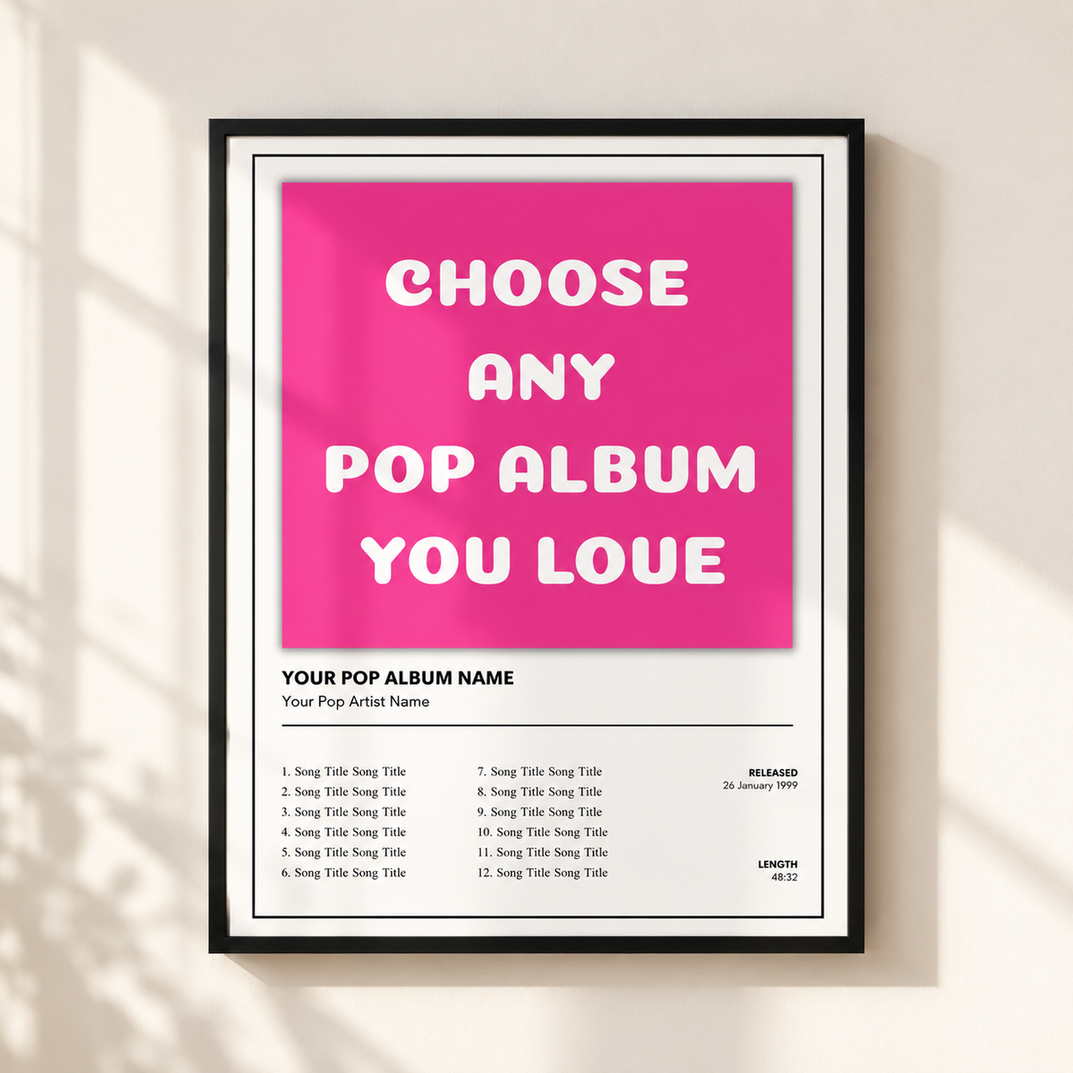 A framed poster print on a light beige wall, featuring a bright pink square with the text 'CHOOSE ANY POP ALBUM YOU LOVE' in large white letters, plus a sample tracklist below.
