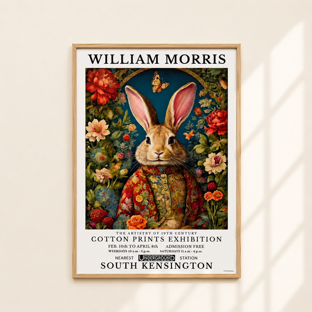 A framed vintage-style poster featuring a rabbit in a floral illustration, hung on a light beige wall with soft window shadows. The poster reads 'WILLIAM MORRIS' at the top and includes exhibition text at the bottom.
