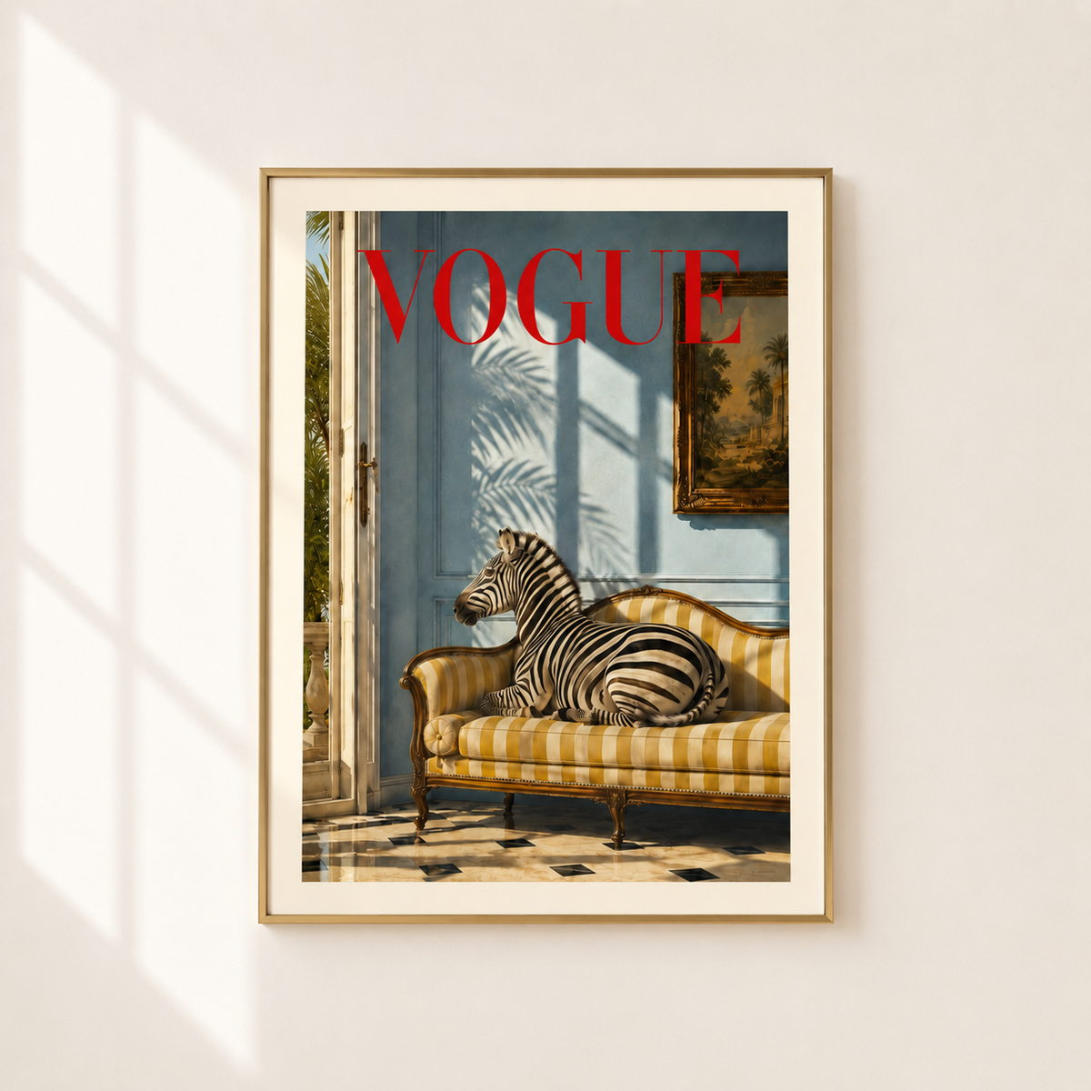 A framed art print featuring a zebra resting on a yellow-and-white striped chaise lounge against a light blue wall, with the word 'VOGUE' in bold red text at the top. The print is mounted in a thin gold frame and hangs on a light beige wall with soft window shadow patterns.