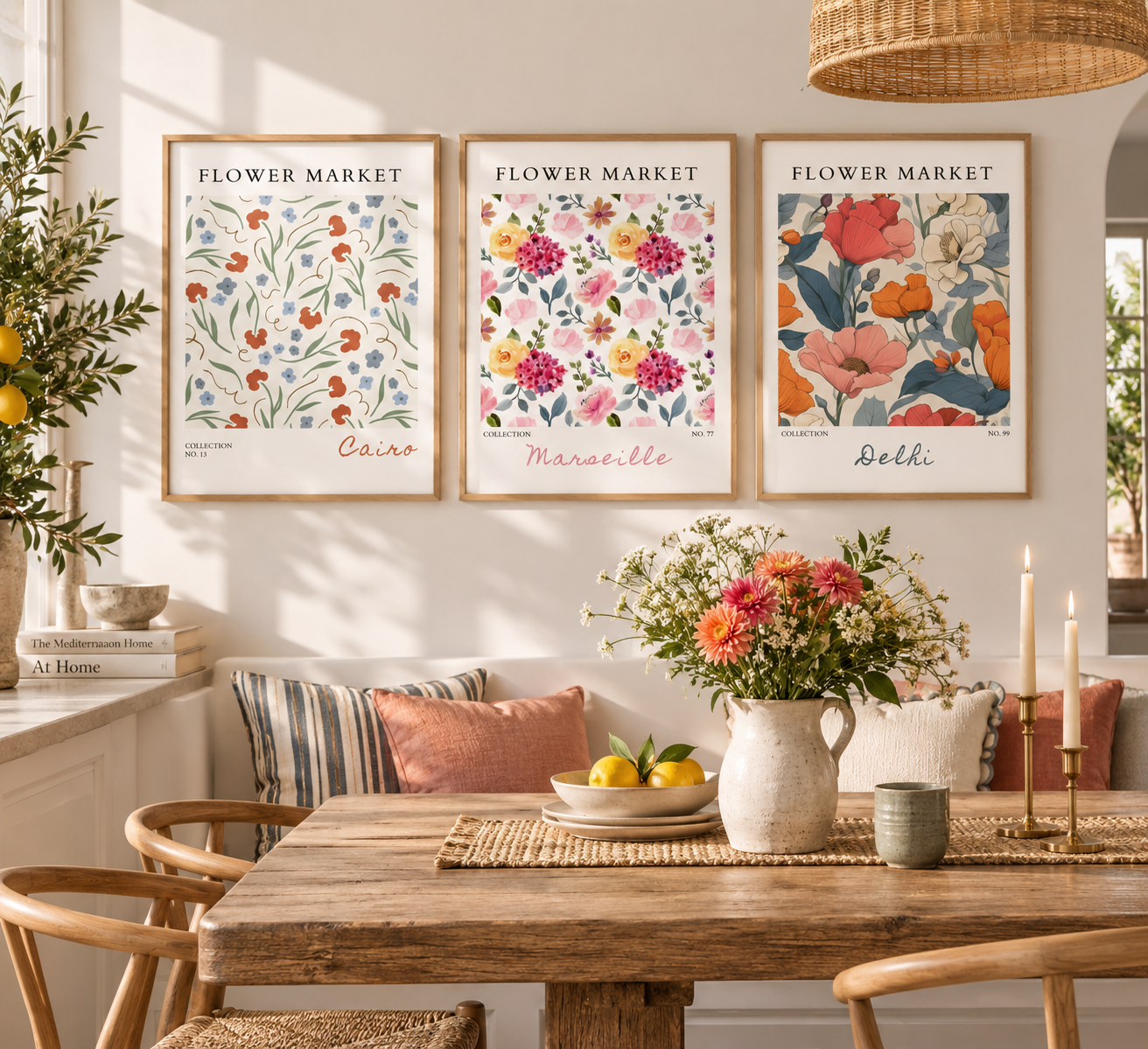 Three framed floral art prints labeled Cairo, Marseille, and Delhi hang on a wall above a rustic dining table with flowers, candles, and pillows in a bright, sunlit room.