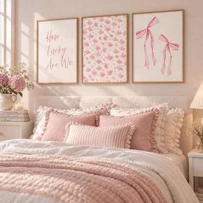 A styled bedroom scene with a bed dressed in blush pink and white bedding, three framed wall art prints above the headboard, and soft natural light from a window.