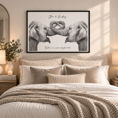 A framed black-and-white elephant artwork hangs above a neatly made bed in a warm, softly lit bedroom. The print shows two elephants facing each other with their trunks touching, with the text 'Jane & Louis' at the top and 'Together is our favorite place to be' at the bottom.