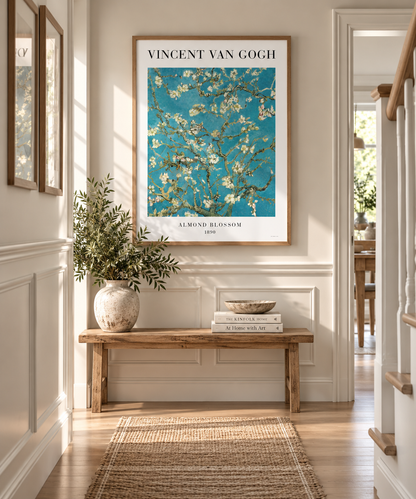 A framed Vincent van Gogh Almond Blossom art print hangs on a cream-colored wall in a bright, modern hallway. The print features a vibrant turquoise blue background with white blossoms and is framed in light wood.