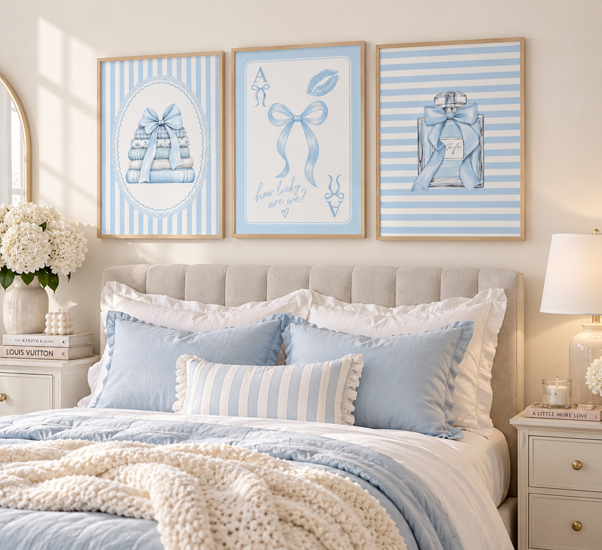Three framed light blue and white decorative wall art prints hang above a neatly made bed with blue pillows, white bedding, and a cream knit throw in a softly lit bedroom.