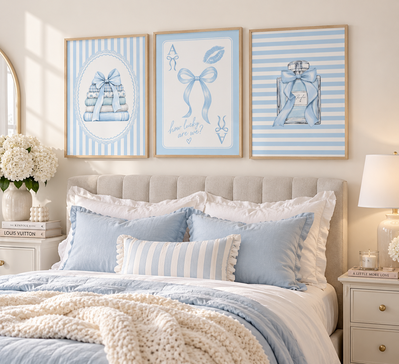 Three framed light blue and white decorative wall art prints hang above a neatly made bed with blue pillows, white bedding, and a cream knit throw in a softly lit bedroom.