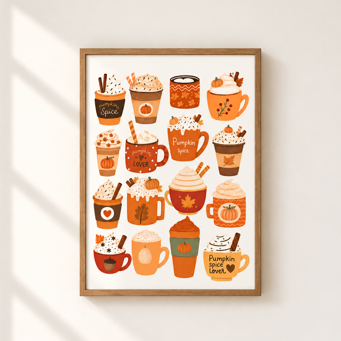 A framed autumn-themed art print featuring 15 cozy illustrated hot cocoa and coffee cups with pumpkins, cinnamon sticks, and fall colors, displayed on a light beige wall with soft window shadow overlays.