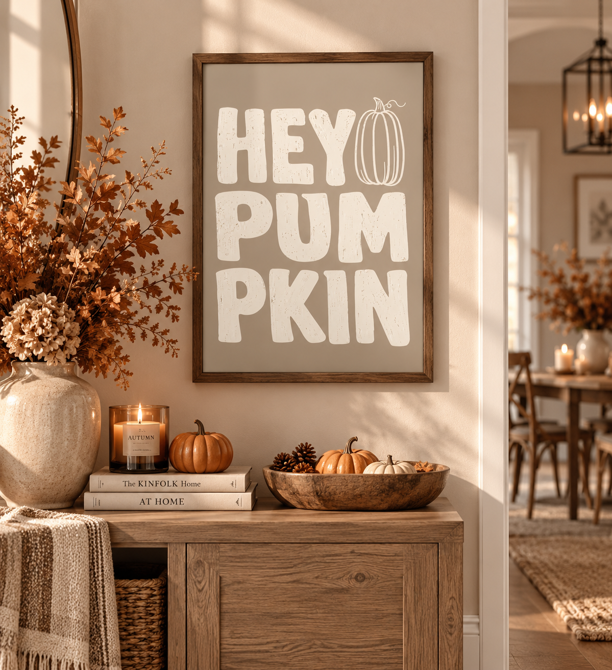 A framed autumn-themed wall sign reading 'HEY PUMPKIN' in white lettering with a pumpkin illustration, displayed in a warm, styled home interior above a wooden console table with fall decor.