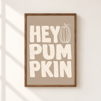 Framed wall art with the phrase “HEY PUMPKIN” in large distressed cream letters on a warm taupe background, with a simple pumpkin illustration integrated into the design. The frame is wood-toned and the print is shown hanging on a light wall with soft window-shadow lighting.