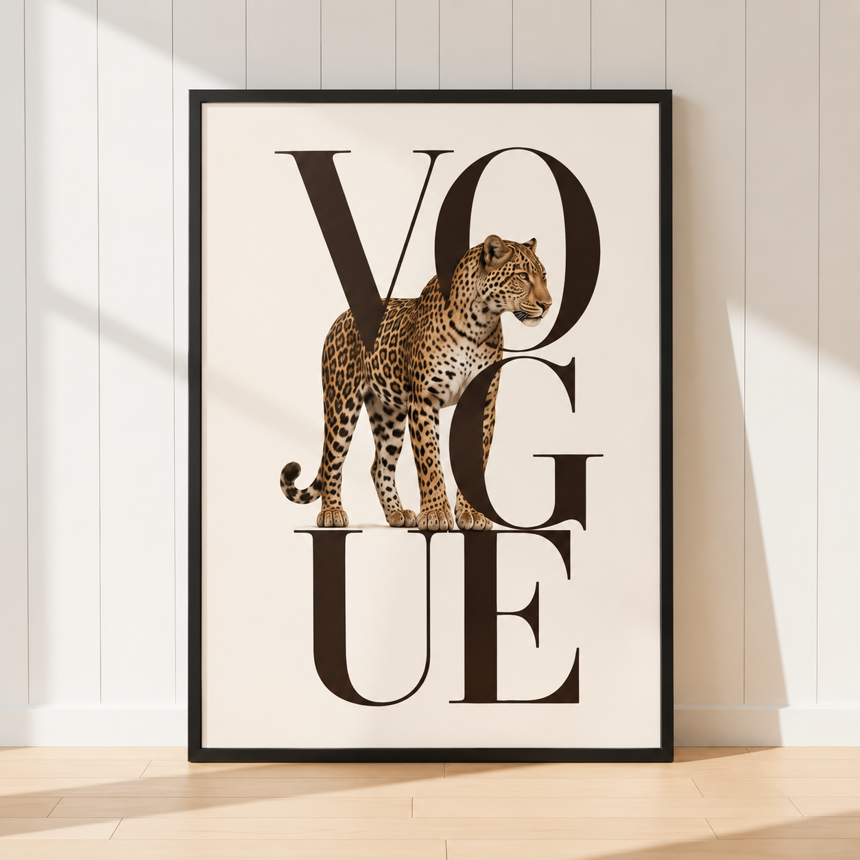 A framed art print featuring a leopard standing behind large black letters spelling VOGUE, leaning against a white paneled wall on a light wood floor.
