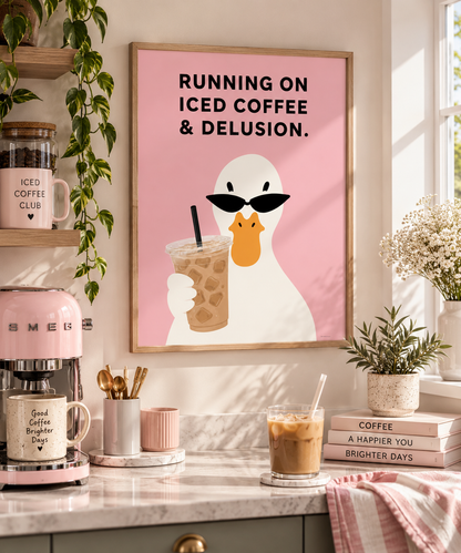 A framed art print featuring a white duck wearing black sunglasses and holding an iced coffee on a pink background, styled on a kitchen wall above a counter with coffee-themed props.