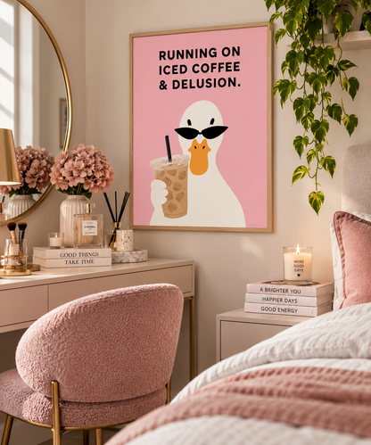 A framed wall art print hangs in a styled bedroom. The print shows a white duck wearing black sunglasses and holding an iced coffee on a pink background, with the text 'RUNNING ON ICED COFFEE & DELUSION.