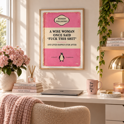 A framed art print with a pink and cream color scheme hangs on a beige wall above a white desk. The print features a quote attributed to 'A Wise Woman' and a small penguin illustration.