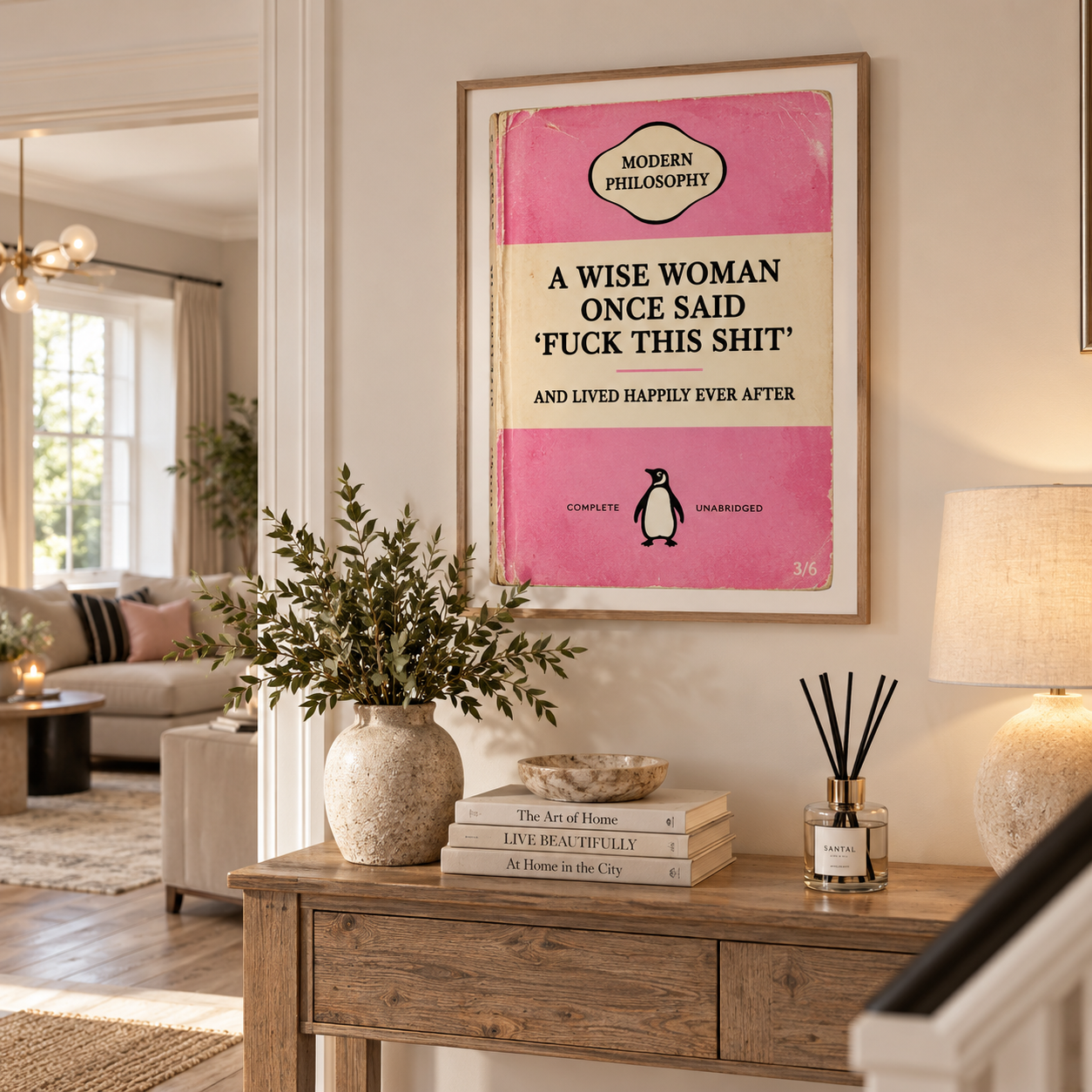 A framed vintage-style book cover print hanging on a beige wall in a styled living space. The print features a pink and cream cover with the text 'A WISE WOMAN ONCE SAID FUCK THIS SHIT AND LIVED HAPPILY EVER AFTER' and a small Penguin logo.