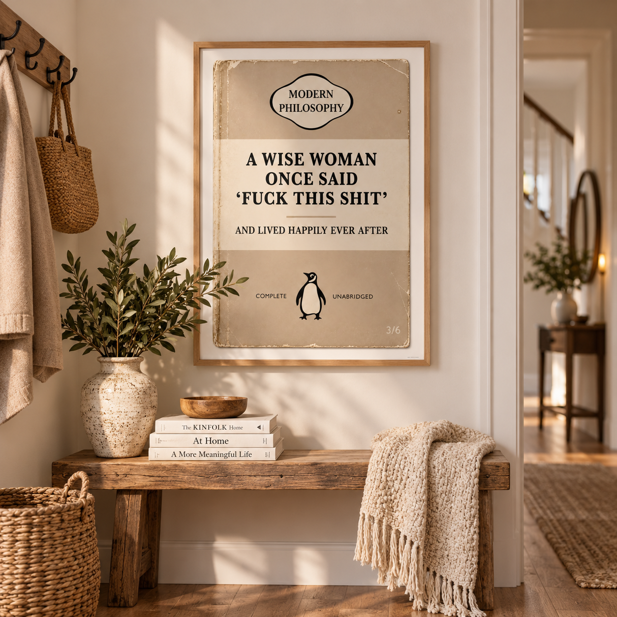A framed vintage-style humorous poster hangs on a beige wall above a rustic wooden bench in a styled home entryway. The poster reads, 'A WISE WOMAN ONCE SAID 'FUCK THIS SHIT' AND LIVED HAPPILY EVER AFTER' with a small penguin illustration.
