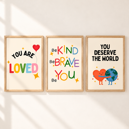 Three framed motivational wall art prints hang side by side on a light wall with soft diagonal shadows. The left print says 'YOU ARE LOVED' with a red heart balloon and multicolor lettering.
