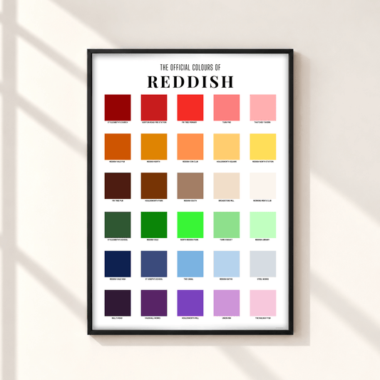 A framed poster titled 'THE OFFICIAL COLOURS OF REDDISH' hangs on a light beige wall. The poster features a grid of 36 color swatches ranging from reds and oranges to greens, blues, purples, and pinks, with labels underneath each square.