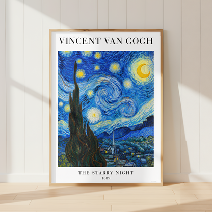 A framed art print of Vincent van Gogh's 'The Starry Night' leaning against a white paneled wall on a light wood floor, with soft sunlight casting shadows.