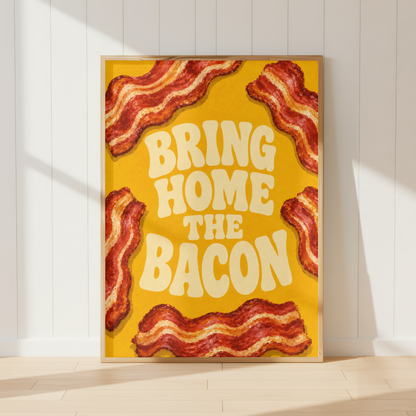A framed art print featuring the phrase 'BRING HOME THE BACON' in cream-colored retro lettering on a bright yellow background, surrounded by illustrated strips of bacon. The framed print is leaning against a white paneled wall on a light wood floor, with soft diagonal shadows cast across the scene.