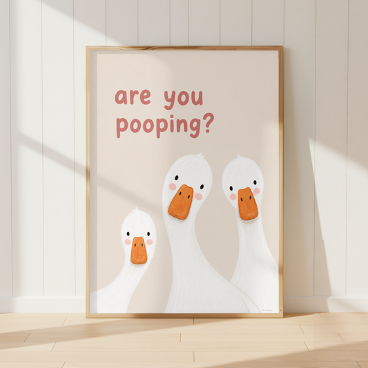 A framed nursery art print leaning against a white paneled wall on a light wood floor. The print features three white cartoon ducks with orange beaks and pink cheeks, with the text 'are you pooping?' in a dusty rose font.