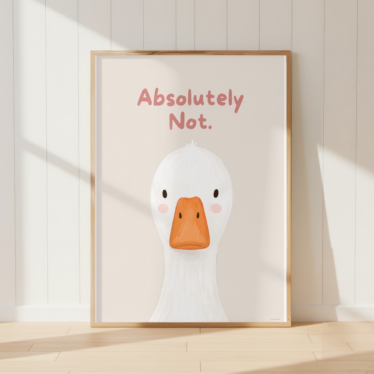 A framed art print featuring a cute white duck illustration with an orange beak and the text 'Absolutely Not.' in pink, leaning against a white paneled wall on a light wood floor.