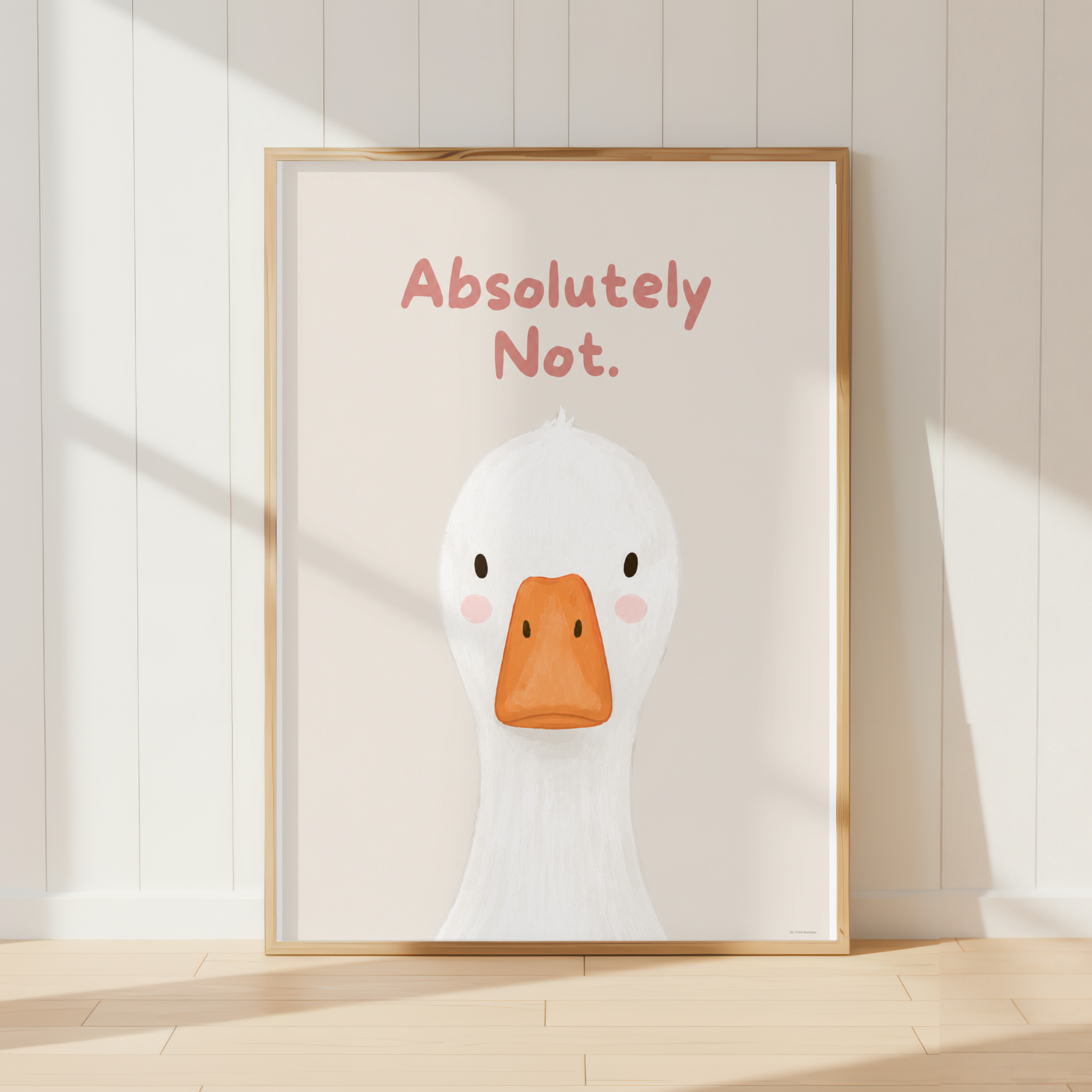 A framed art print featuring a cute white duck illustration with an orange beak and the text 'Absolutely Not.' in pink, leaning against a white paneled wall on a light wood floor.