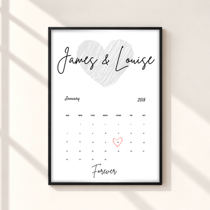 A personalized framed calendar print on a light beige wall with soft diagonal shadows. The print features a white background, a black frame, a hand-drawn gray heart, the names 'James & Louise' in black script, a January 2018 calendar grid, and 'Forever' written at the bottom, with the number 1 highlighted in red.
