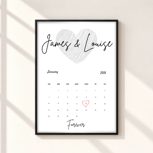 A personalized framed calendar print on a light beige wall with soft diagonal shadows. The print features a white background, a black frame, a hand-drawn gray heart, the names 'James & Louise' in black script, a January 2018 calendar grid, and 'Forever' written at the bottom, with the number 1 highlighted in red.