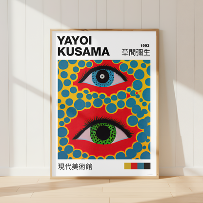 A framed art print of Yayoi Kusama's 1993 exhibition poster, leaning against a white paneled wall on a light wood floor. The poster features two stylized eyes with red, blue, green, and yellow patterns.