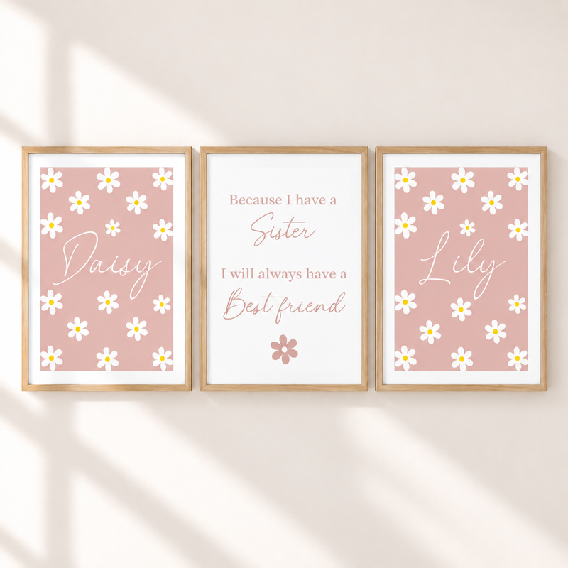 Three framed personalized nursery art prints on a warm beige wall with soft diagonal shadows. The left print says 'Daisy' with white daisies on a dusty pink background, the center print reads 'Because I have a Sister I will always have a Best friend' on a white background, and the right print says 'Lily' with white daisies on a dusty pink background.
