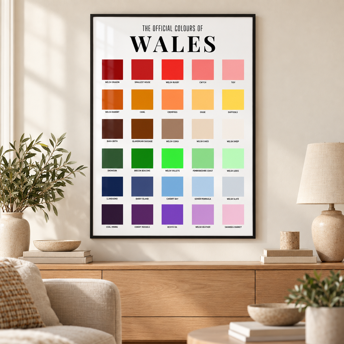
Wales colour chart print in a thin black frame above an oak sideboard in a neutral lounge, featuring 30 colourful squares with Welsh-themed labels.