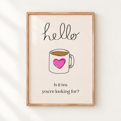 A framed typographic art print featuring a hand-drawn coffee mug with a pink heart, the word 'hello' at the top, and the phrase 'Is it tea you're looking for?' at the bottom, shown hanging on a light wall.