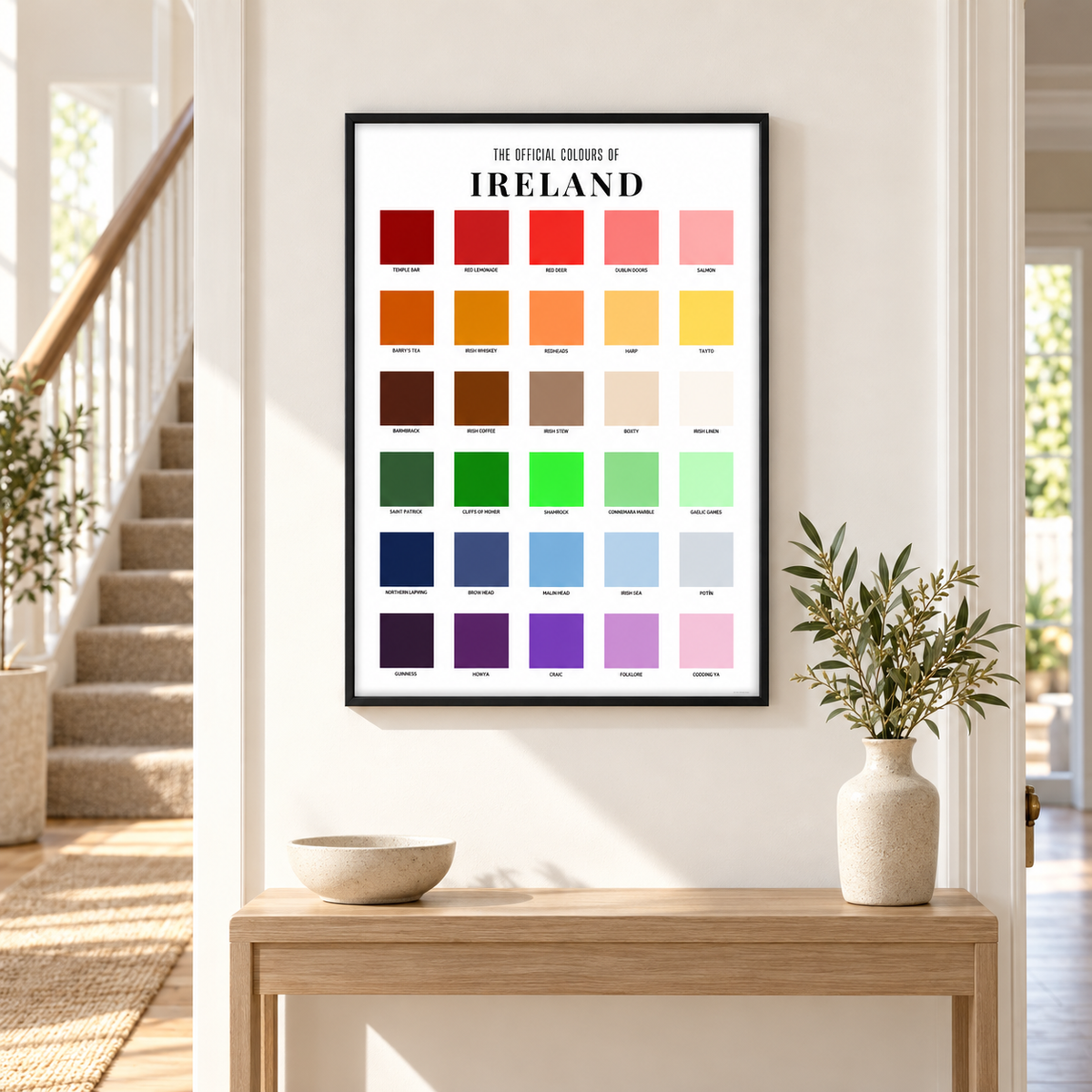 A framed poster titled 'THE OFFICIAL COLOURS OF IRELAND' hangs on a white wall above a light wood console table. The poster features a grid of colorful color swatches representing the Irish flag and landscape.