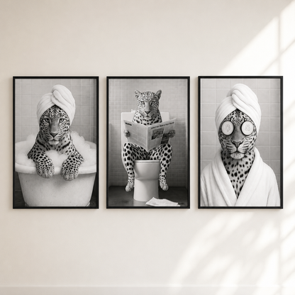 Three framed black-and-white animal wall art prints hang side by side on a light wall. The left print shows a leopard in a bathtub, the center shows a leopard sitting on a toilet reading a newspaper, and the right print shows a leopard with a towel and round eye mask.