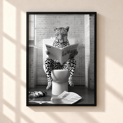 A framed black and white art print hanging on a beige wall, showing a leopard sitting on a toilet and reading a newspaper in a tiled bathroom.