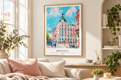 A framed art print of a Madrid street scene hangs on a beige wall in a modern living room setting with a sofa, plants, and shelves.