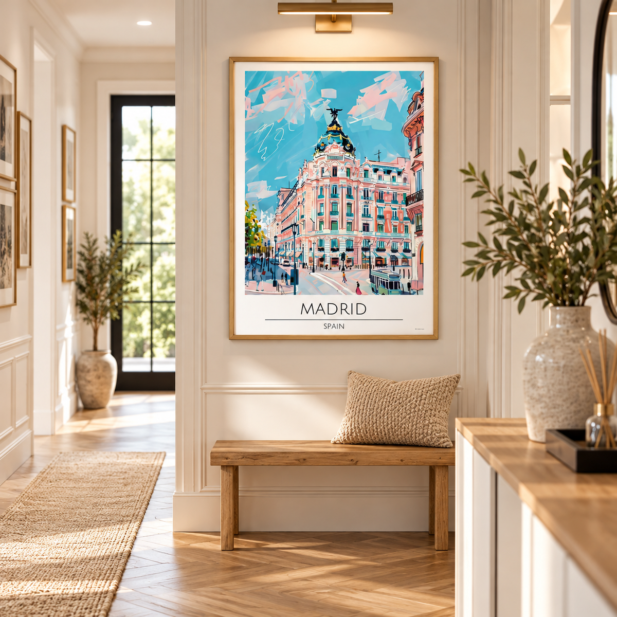A framed travel poster of Madrid, Spain, hanging on a white wall in a bright, modern hallway. The poster features a colorful illustration of a classic Madrid building under a blue sky, with 'MADRID' and 'SPAIN' printed at the bottom.