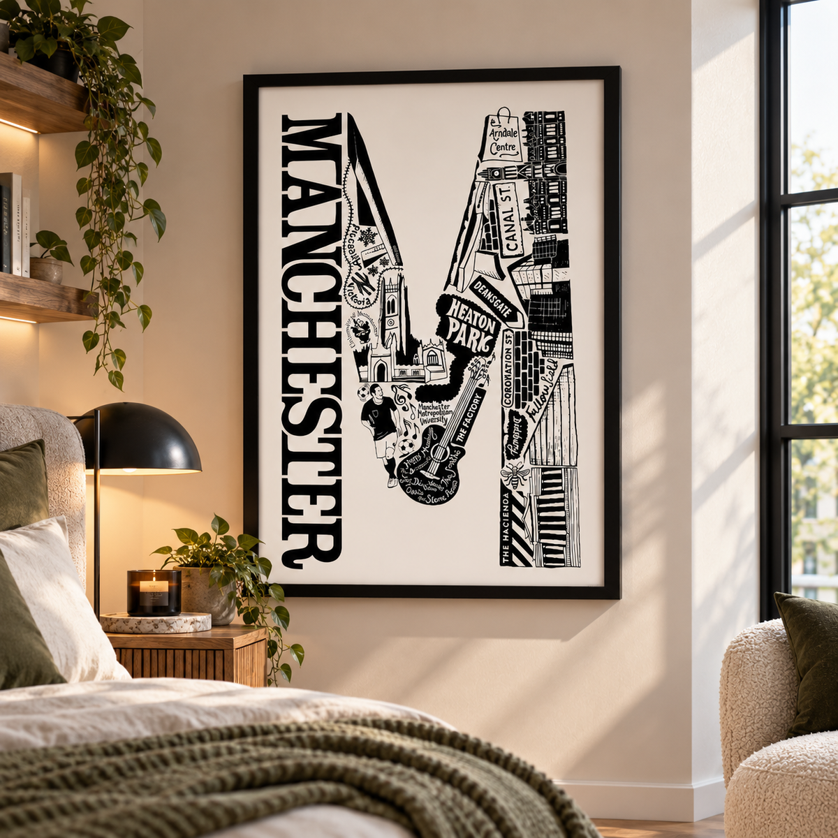A framed black and white Manchester cityscape art print hangs on a beige wall in a modern bedroom setting with a bed, bedside lamp, and window visible.